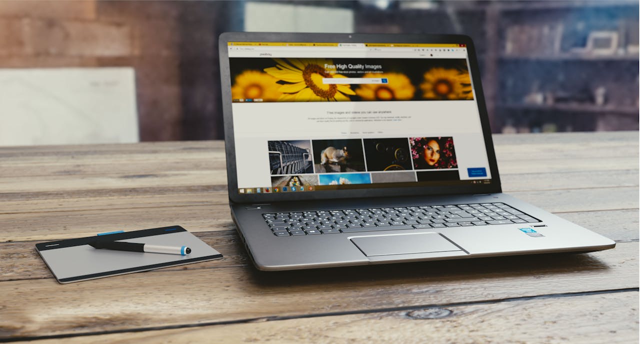 home-img Laptop with open webpage on wooden desk, accompanied by tablet and pen, representing digital work setup.